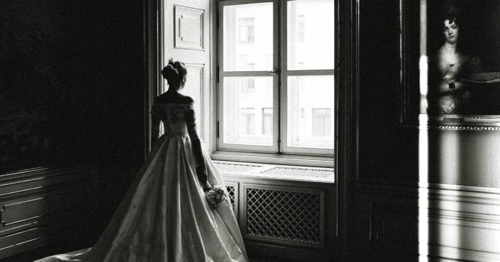 This is a wedding photo idea of a black and white image of a bride gazing out of a picturesque window